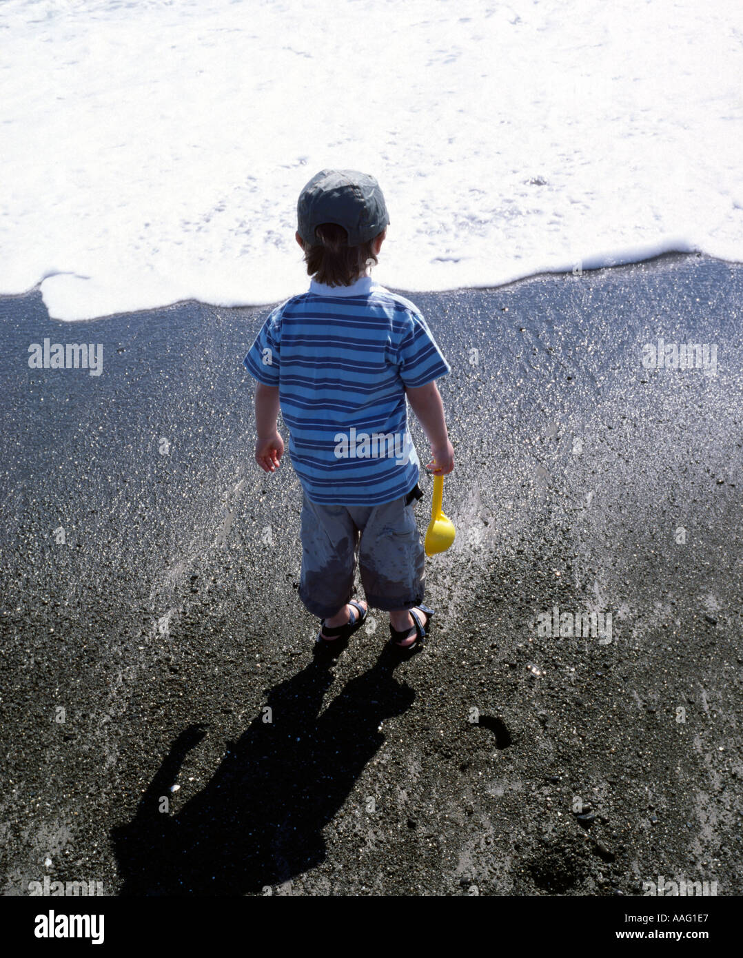 boy with spade watching incoming wave at beach Stock Photo - Alamy