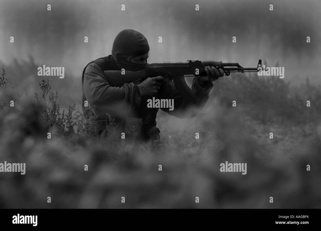 a terrorist dressed in a balaclava firing an AK47 kalashnikov rifle and wearing a belt of bullets Stock Photo
