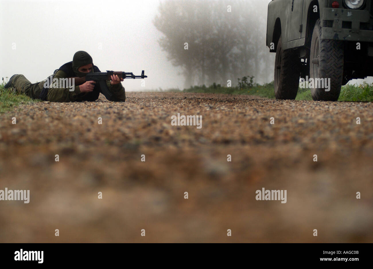 a terrorist dressed in a balaclava holding an AK47 kalashnikov rifle and wearing a belt of bullets next to a land rover POSED BY MODEL Stock Photo