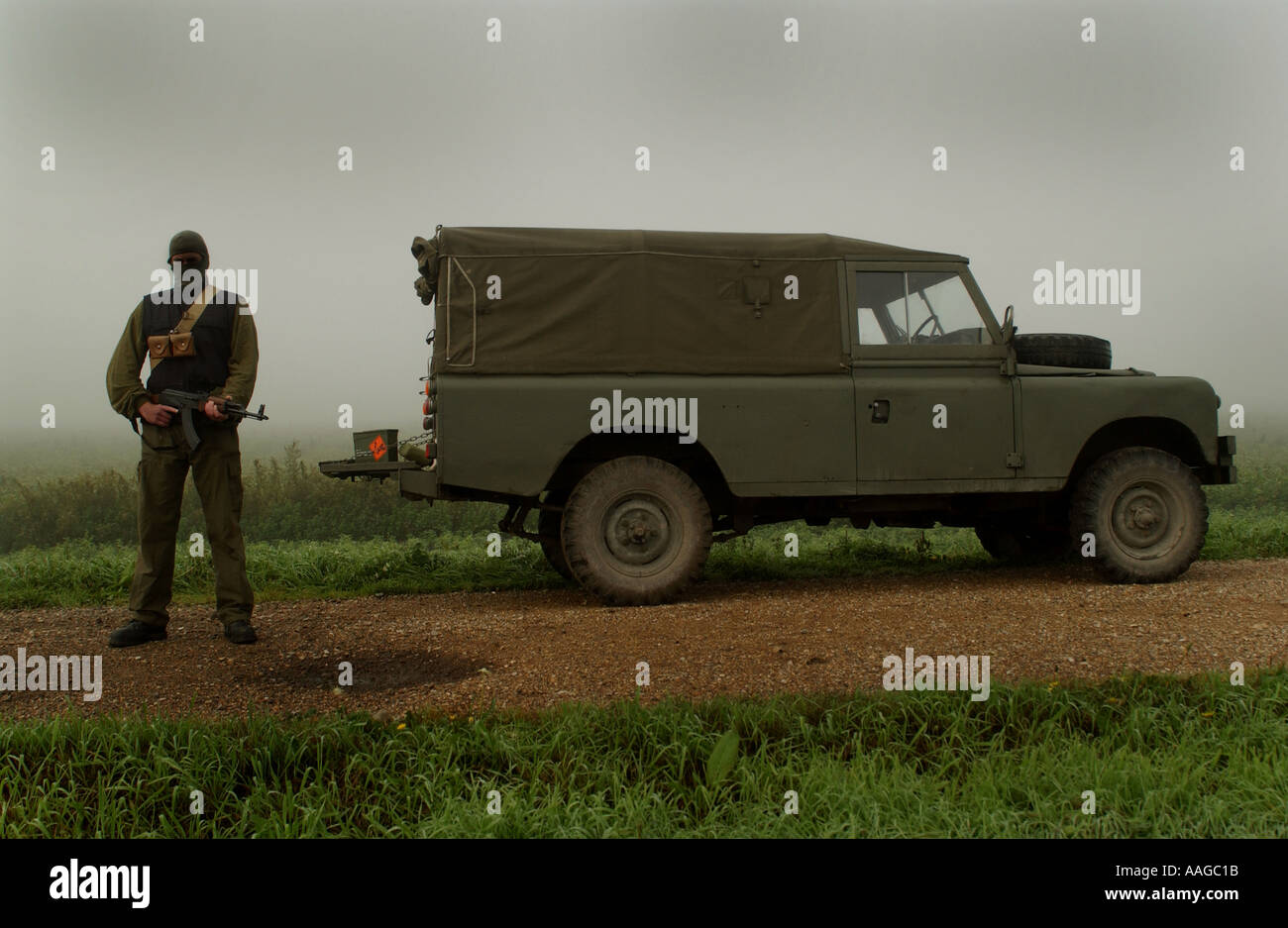 a terrorist dressed in a balaclava holding an AK47 kalashnikov rifle and wearing a belt of bullets next to a land rover POSED BY MODEL Stock Photo