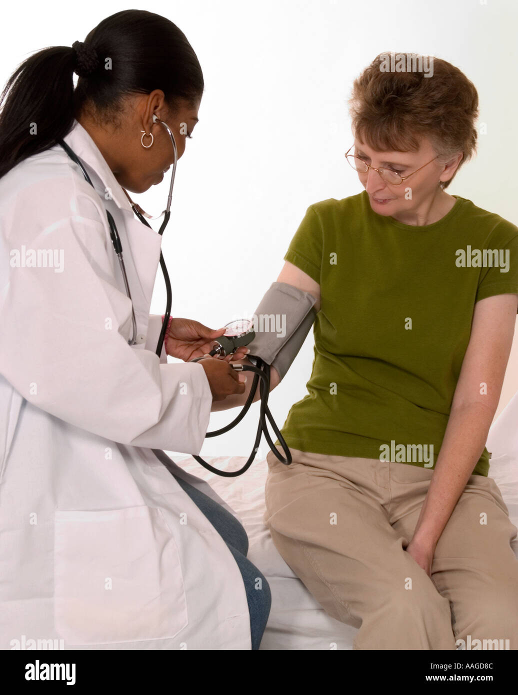 African American GP  (25 - 30) checking blood pressure of Caucasian Senior Female  (age 60-70) . Stock Photo