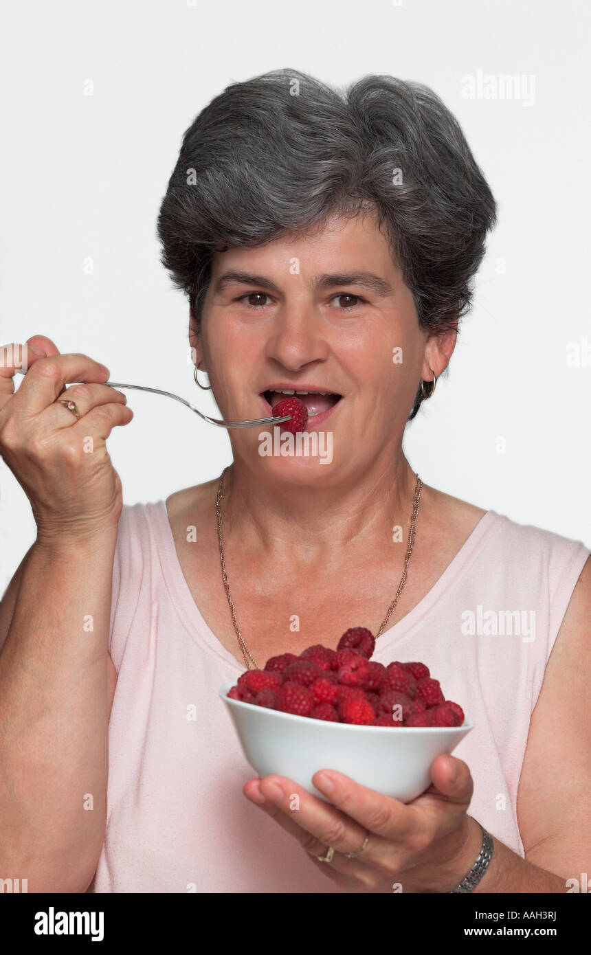Mature woman eating bowl of raspberries portrait close up Stock Photo ...