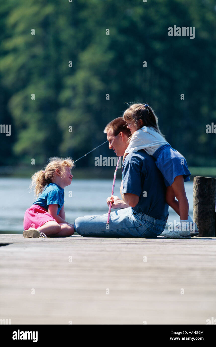 Father sitting with daughters on pier by lake Stock Photo