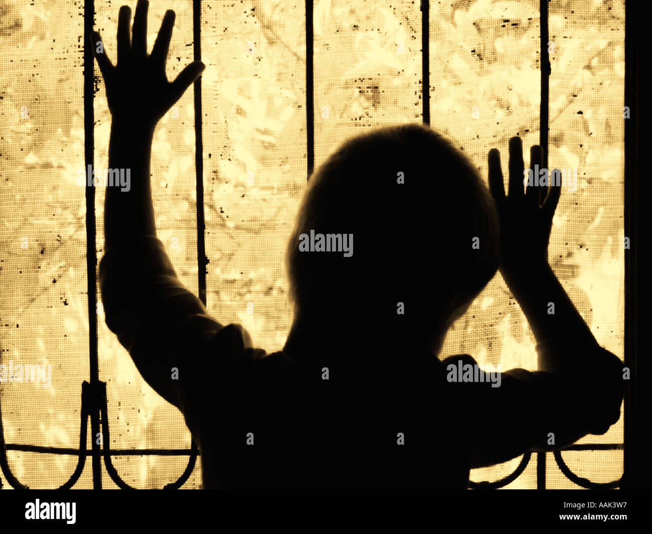 Little boy silhouetted behind the bars of a window Stock Photo