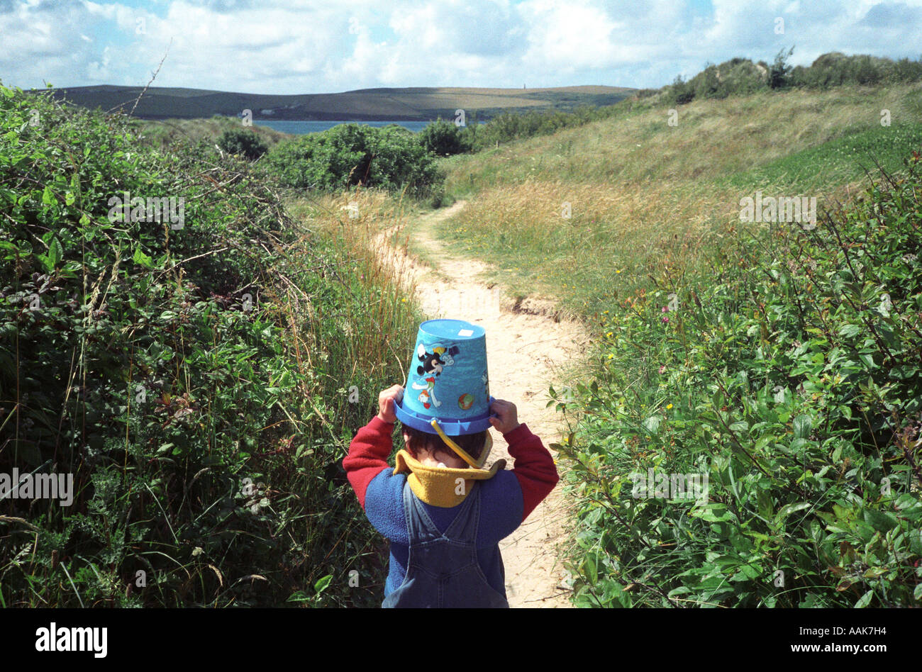 A young boy carries a bucket on his head whilst walking along a coastal path, Rock, Cornwall, UK. Stock Photo