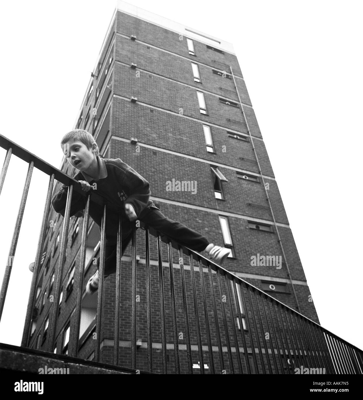 A young boy hurdles over a metal fence below the tower block in which he lives, Clapton, Hackney, London, UK. Stock Photo