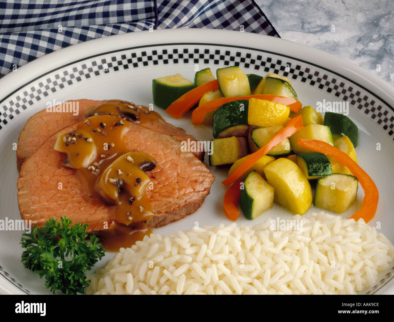 Beef tenderloin with brown mushroom gravy served with zucchini and orange bell pepper with white rice with parsley garnish Stock Photo