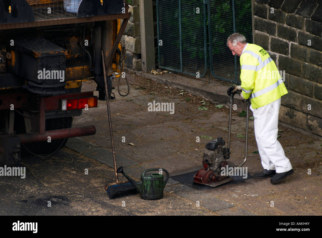 Workman repairing a flagged footpath with tarmacadam Stock Photo