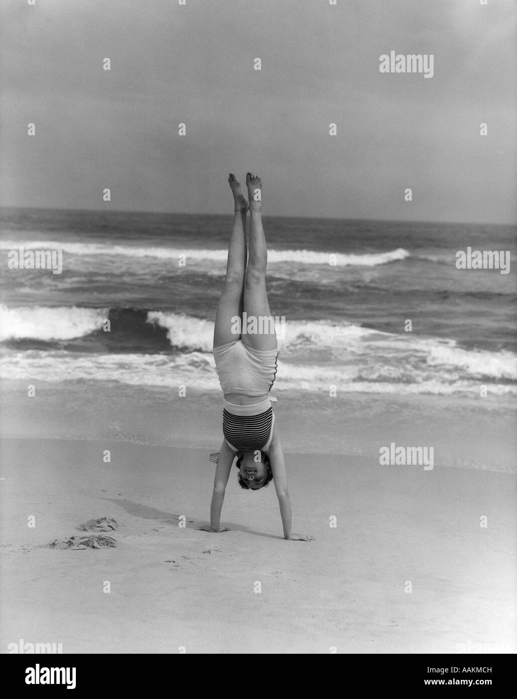 1930s WOMAN DOING HANDSTAND ON BEACH UPSIDE DOWN EXERCISE Stock Photo