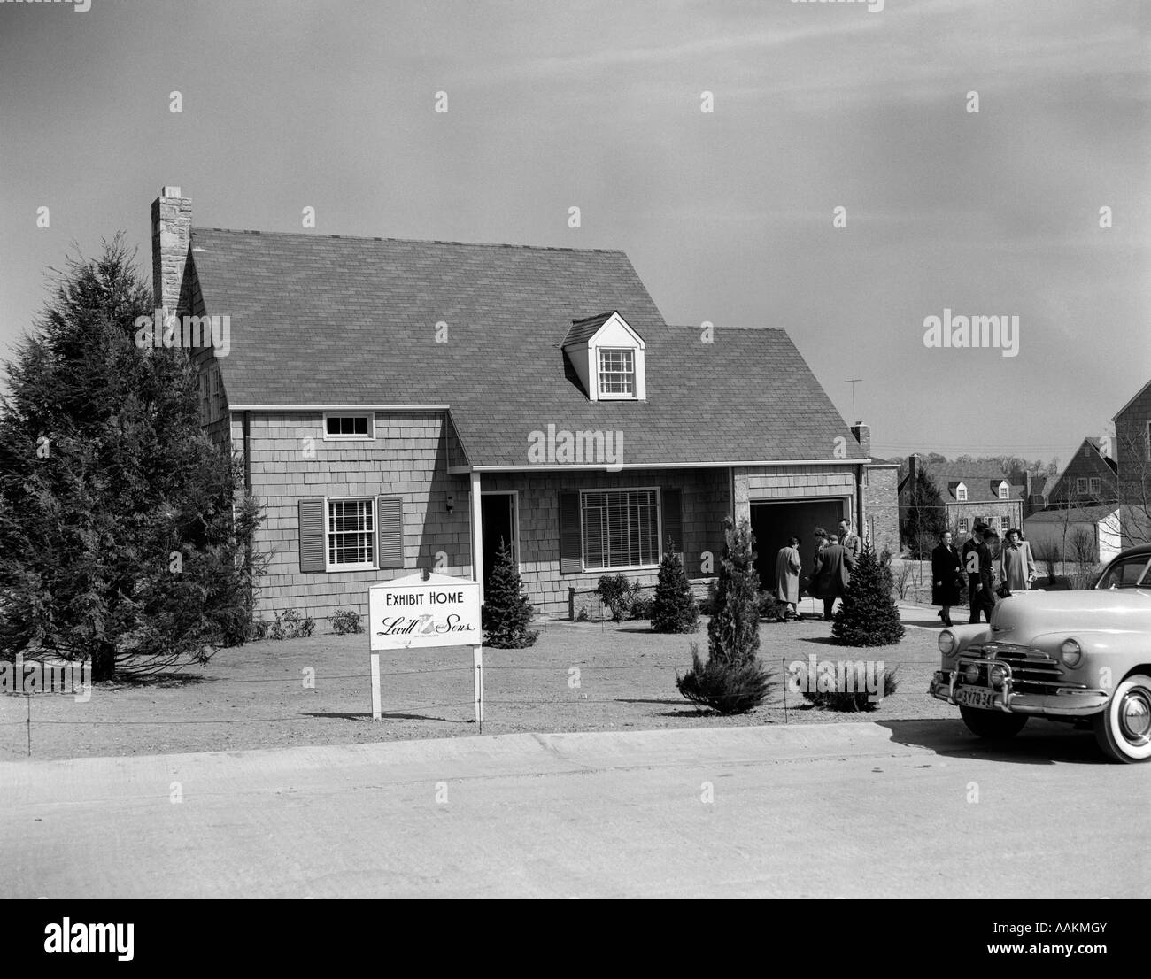 1940s 1950s LEVITTOWN MODEL HOME WITH SIGN OF LEVITT & SONS EXHIBIT HOME WITH PEOPLE MILLING ABOUT Stock Photo