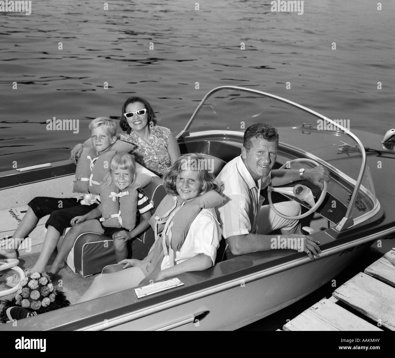 1960s SMILING FAMILY OF FIVE IN DOCKED BOAT CHILDREN WEARING LIFE VESTS LOOKING AT CAMERA Stock Photo