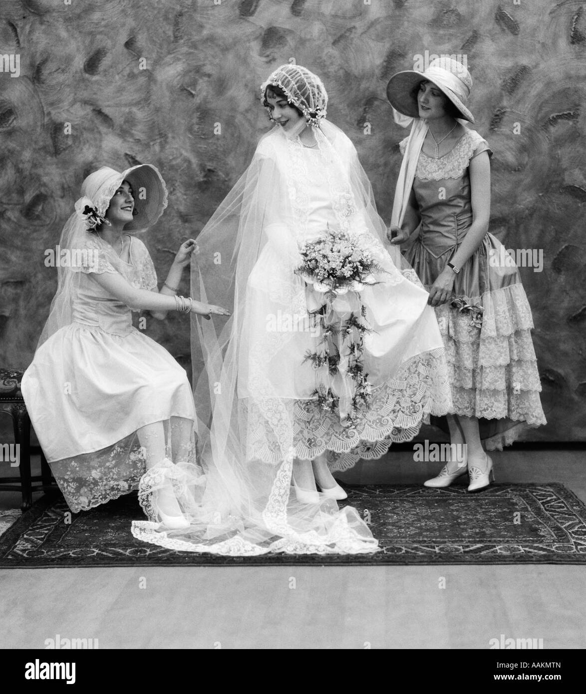 1900 1910s BRIDE WITH ONE BRIDESMAID ON EITHER SIDE HELPING FIX HER WEDDING DRESS Stock Photo