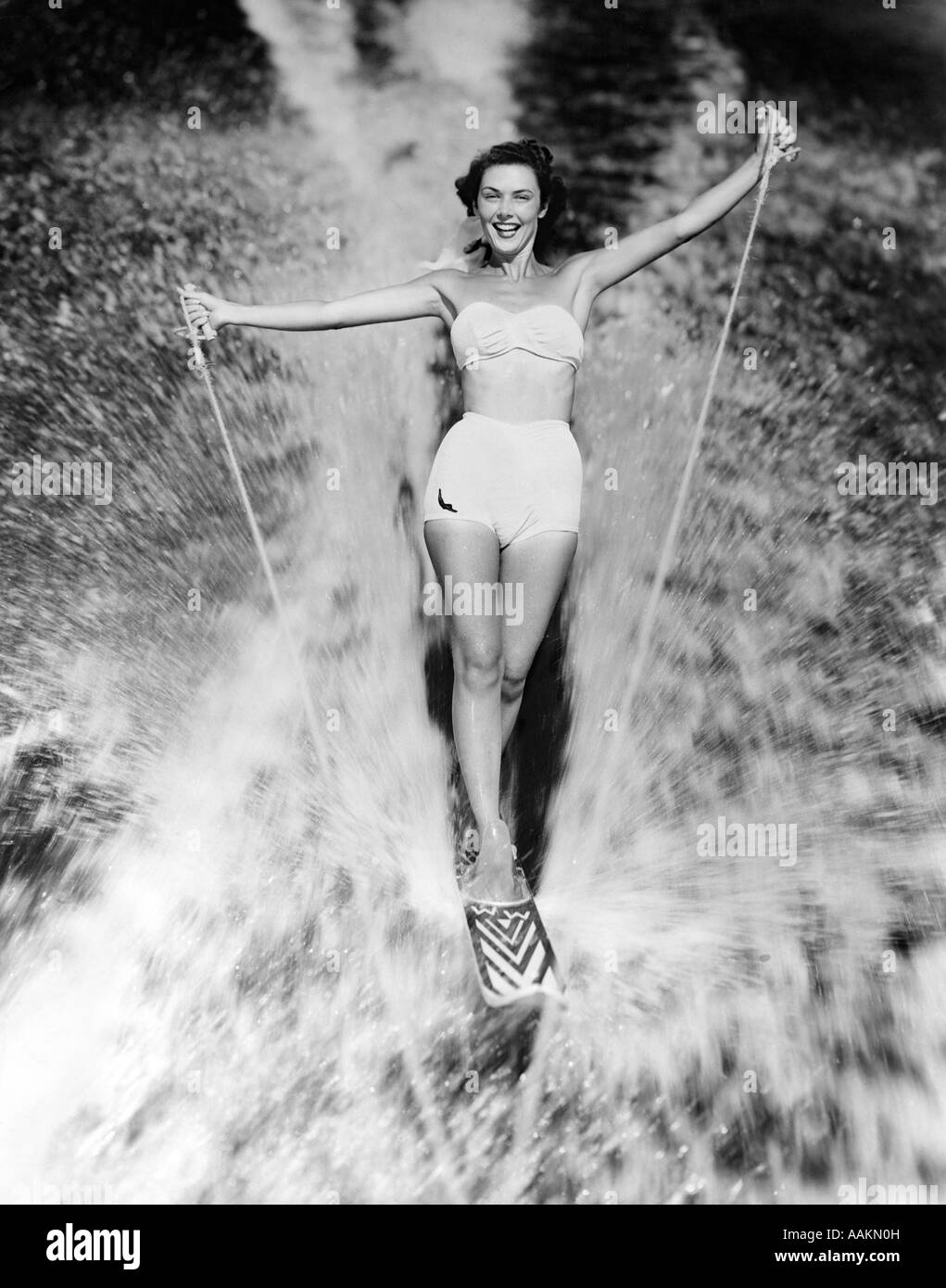 1950s SMILING WOMAN IN WHITE TWO PIECE BATHING SUIT AQUAPLANING WATER SKIING LOOKING AT CAMERA Stock Photo