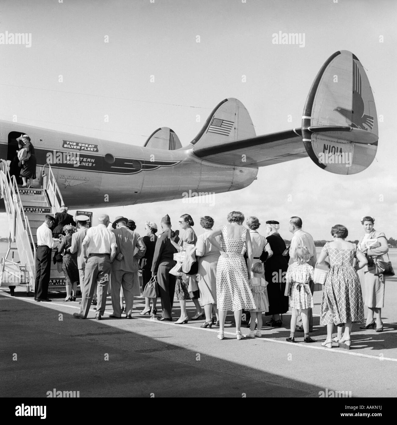 1950s TAIL OF COMMERCIAL AVIATION AIRPLANE ON TARMAC WITH PASSENGERS IN 