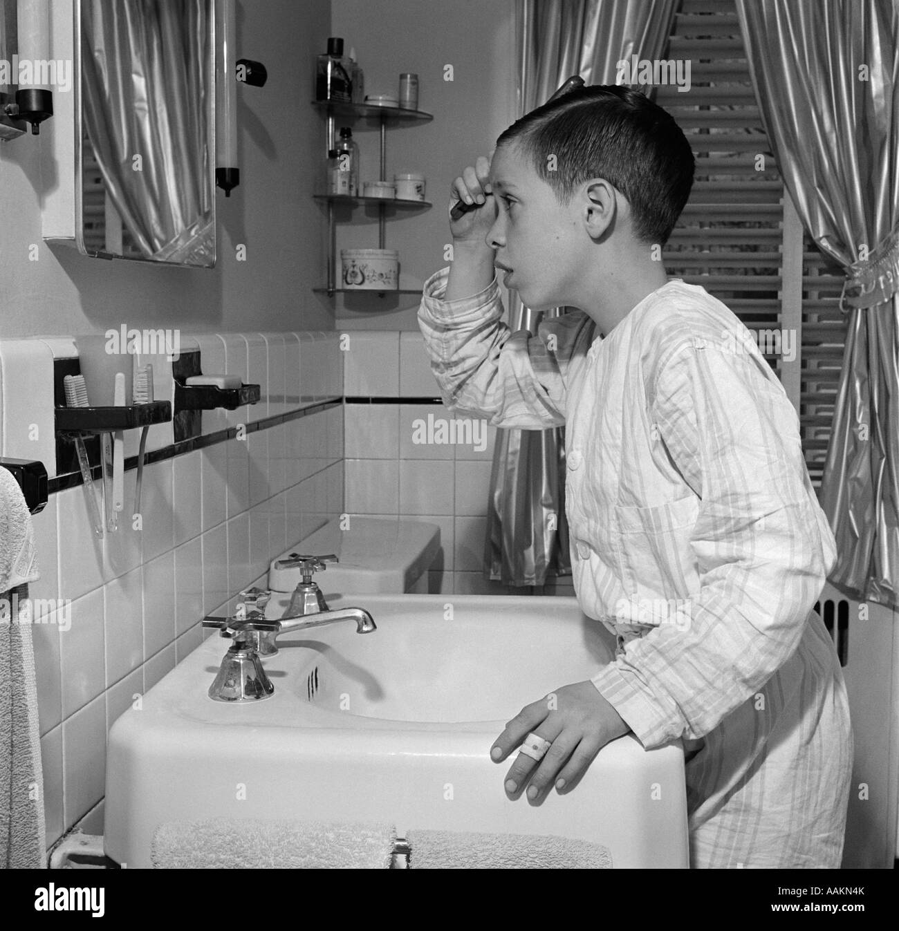 1950s BOY COMBING HAIR LOOKING IN BATHROOM SINK MIRROR Stock Photo