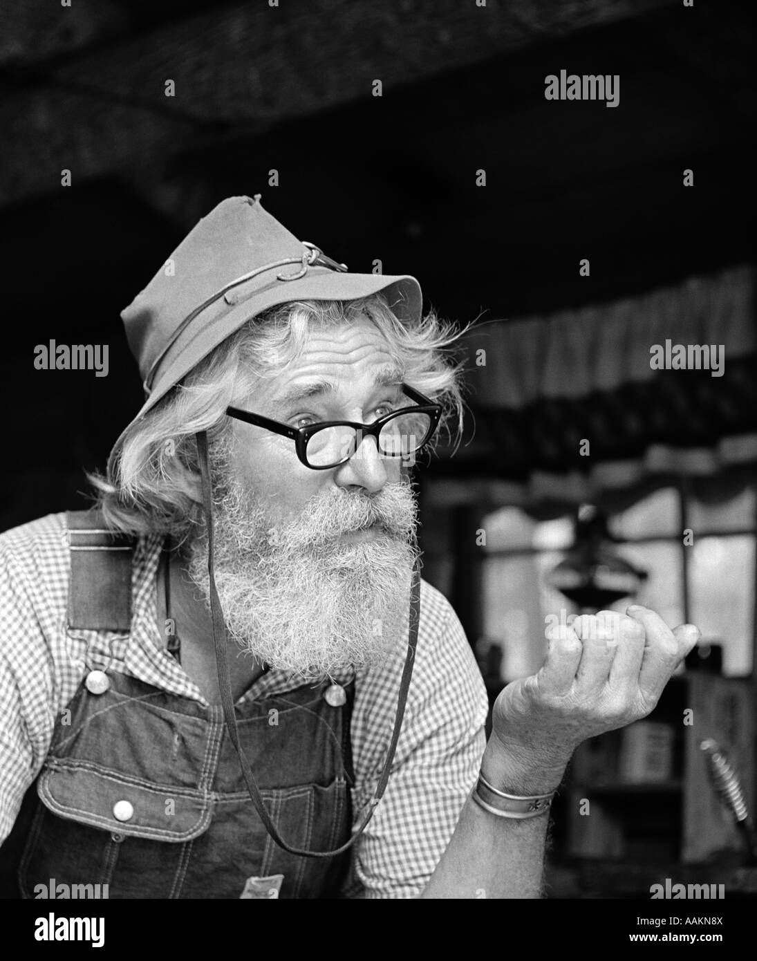 1970s OLDER MAN MOUNTAIN CRAFTSMAN CHARACTER WEARING FELT HAT COTTON OVERALLS GINGHAM SHIRT WITH GLASSES BEARD OUTDOOR Stock Photo