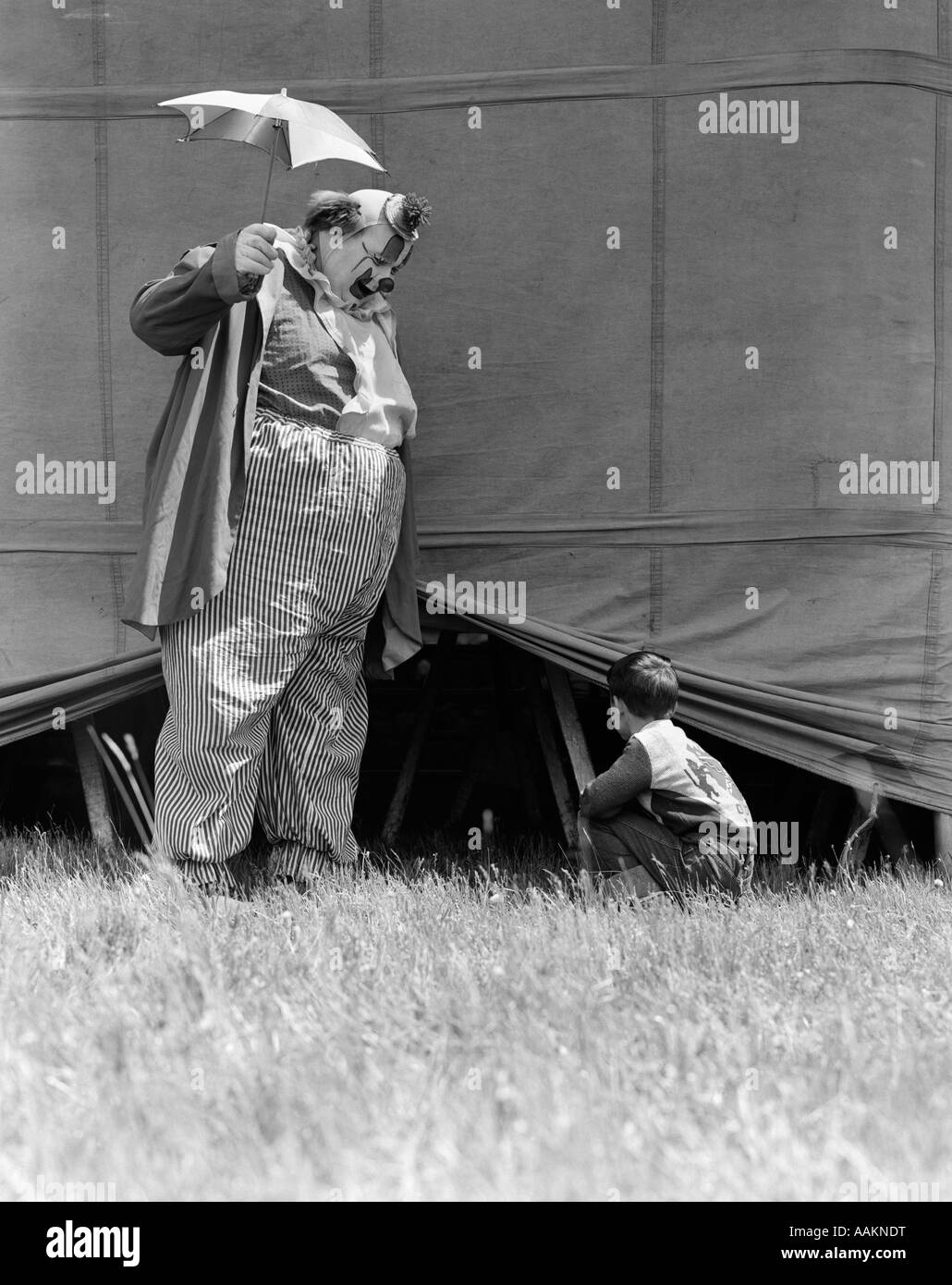1930s MAN CLOWN CATCHING LITTLE BOY PEEKING UNDER CIRCUS BIG TOP TENT Stock Photo