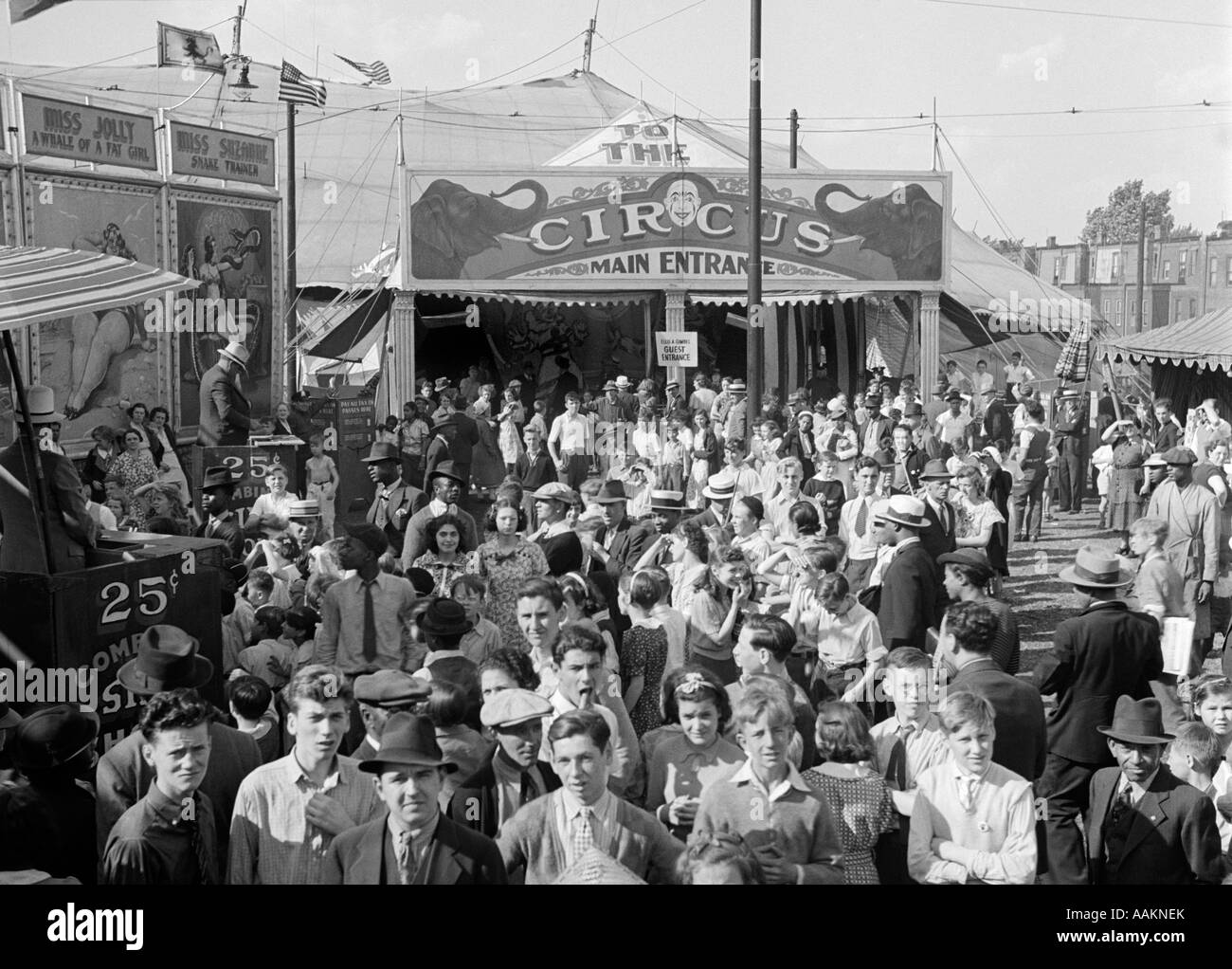 1940s CROWD OF PEOPLE MEN WOMEN CHILDREN CROWDING THE MIDWAY OUTSIDE THE MAIN ENTRANCE TO THE BIG TOP CIRCUS TENT Stock Photo