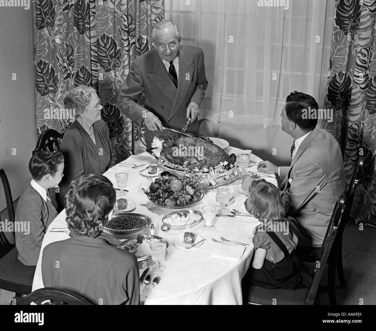 1940s 1950s 3 GENERATION FAMILY MEAL DINING ROOM TABLE GRANDFATHER CARVING TURKEY Stock Photo
