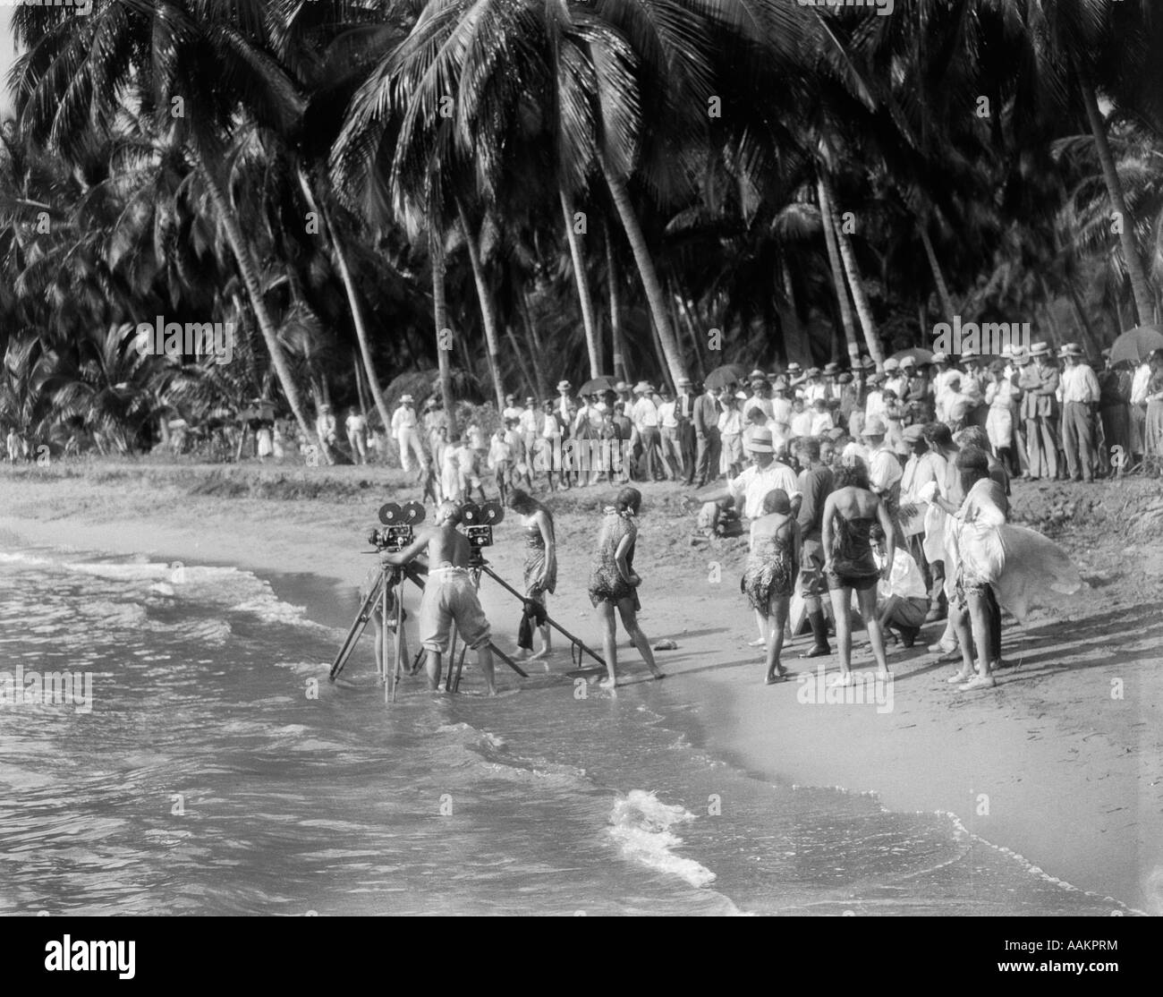 1920s MOVIE CREW WITH CAMERAS ON TRIPODS IN SURF ON TROPICAL BEACH Stock Photo