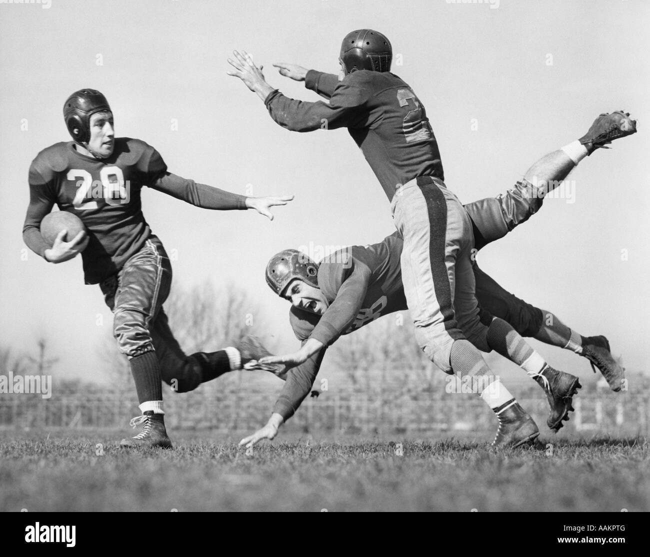 1940s THREE MEN PLAYING FOOTBALL LEATHER HELMETS ONE BLOCKING TACKLER WHO IS TRYING TO CATCH BALL CARRIER Stock Photo