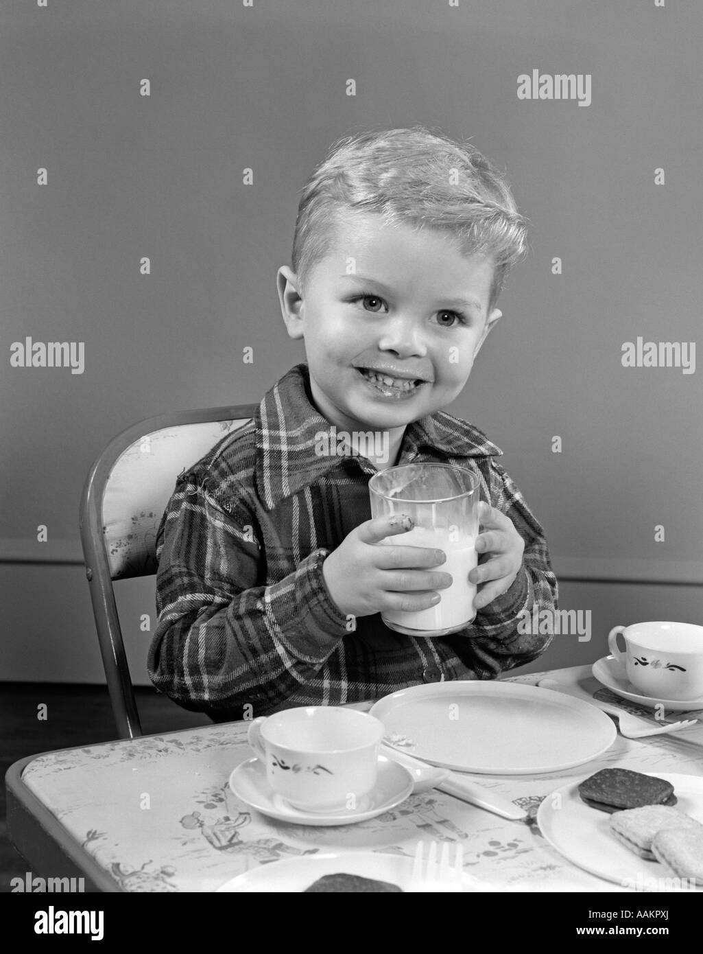1950s SMILING BOY IN PLAID SHIRT DRINKING MILK AT TABLE LOOKING AT CAMERA Stock Photo