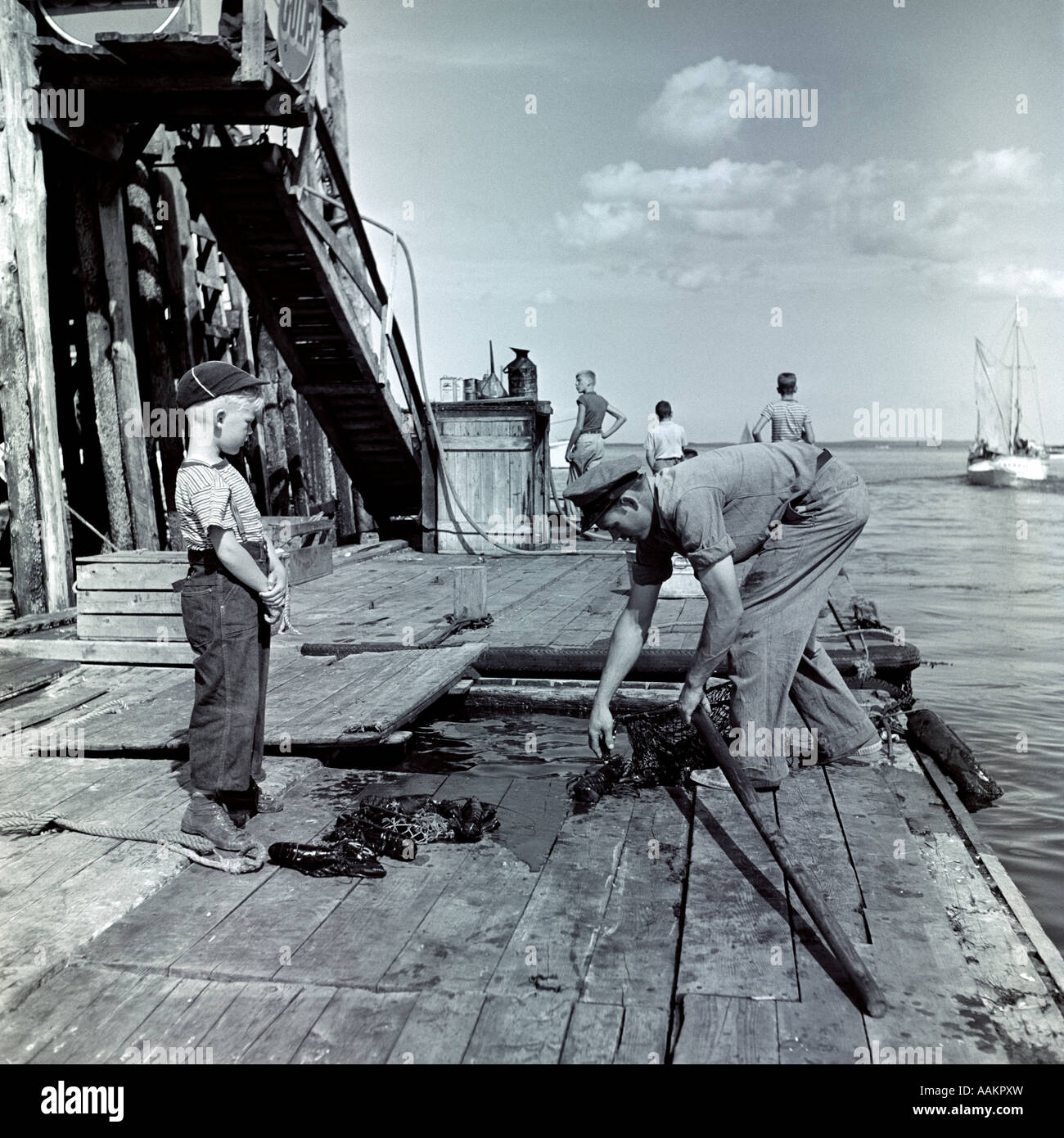 1930s LITTLE BOY WATCHING FISHERMAN UNLOADING LOBSTERS FROM PEN ON DOCK