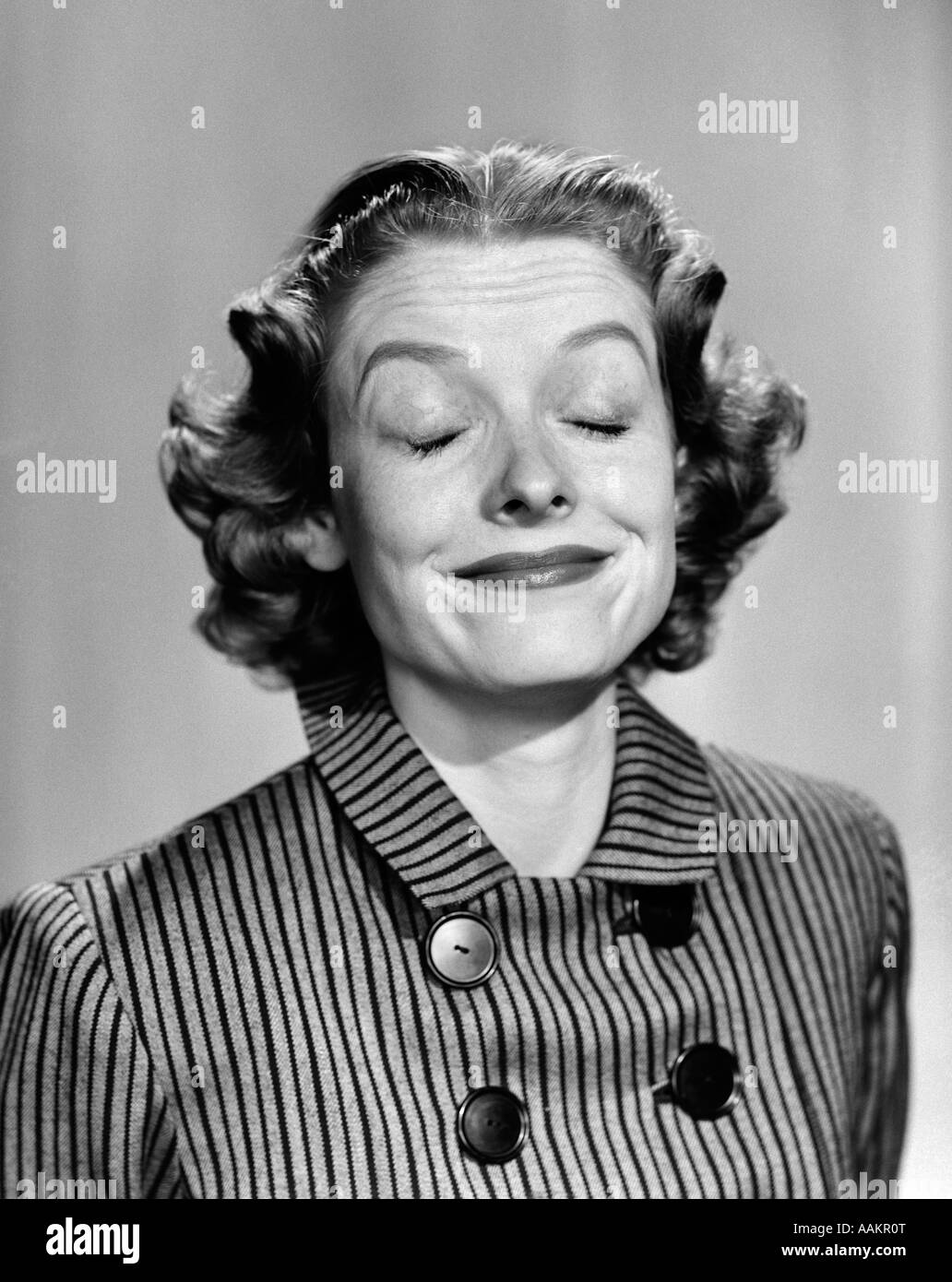 1950s 1960s PORTRAIT WOMAN SMILING EYES CLOSED MAKING A FUNNY FACE WEARING A STRIPED DRESS WITH BUTTONS Stock Photo