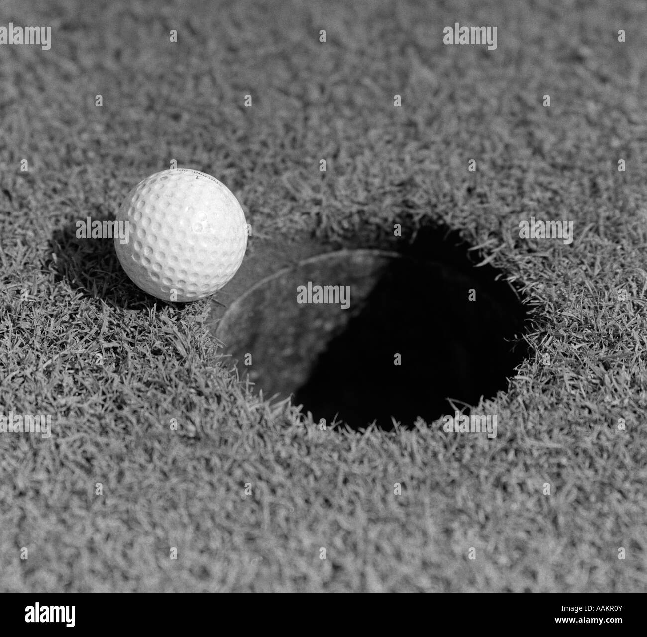 1950s CLOSE-UP OF GOLF BALL ON GREEN ON VERY EDGE OF CUP Stock Photo