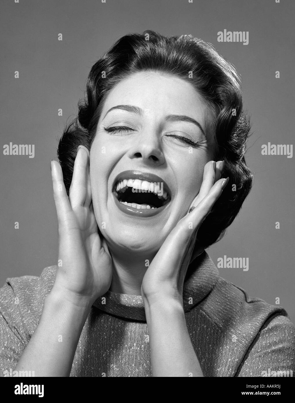 1950s 1960s HAPPY BRUNETTE WOMAN SMILING LAUGHING YELLING HANDS TO CHEEKS EYES CLOSED Stock Photo