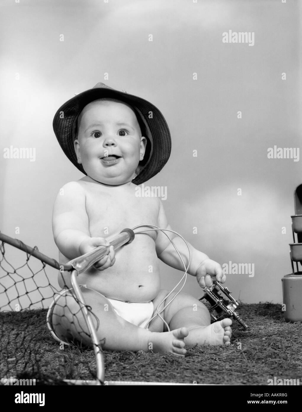 1960s BABY GIRL WEARING FISHING HAT HOLDING NET AND REEL FISHING