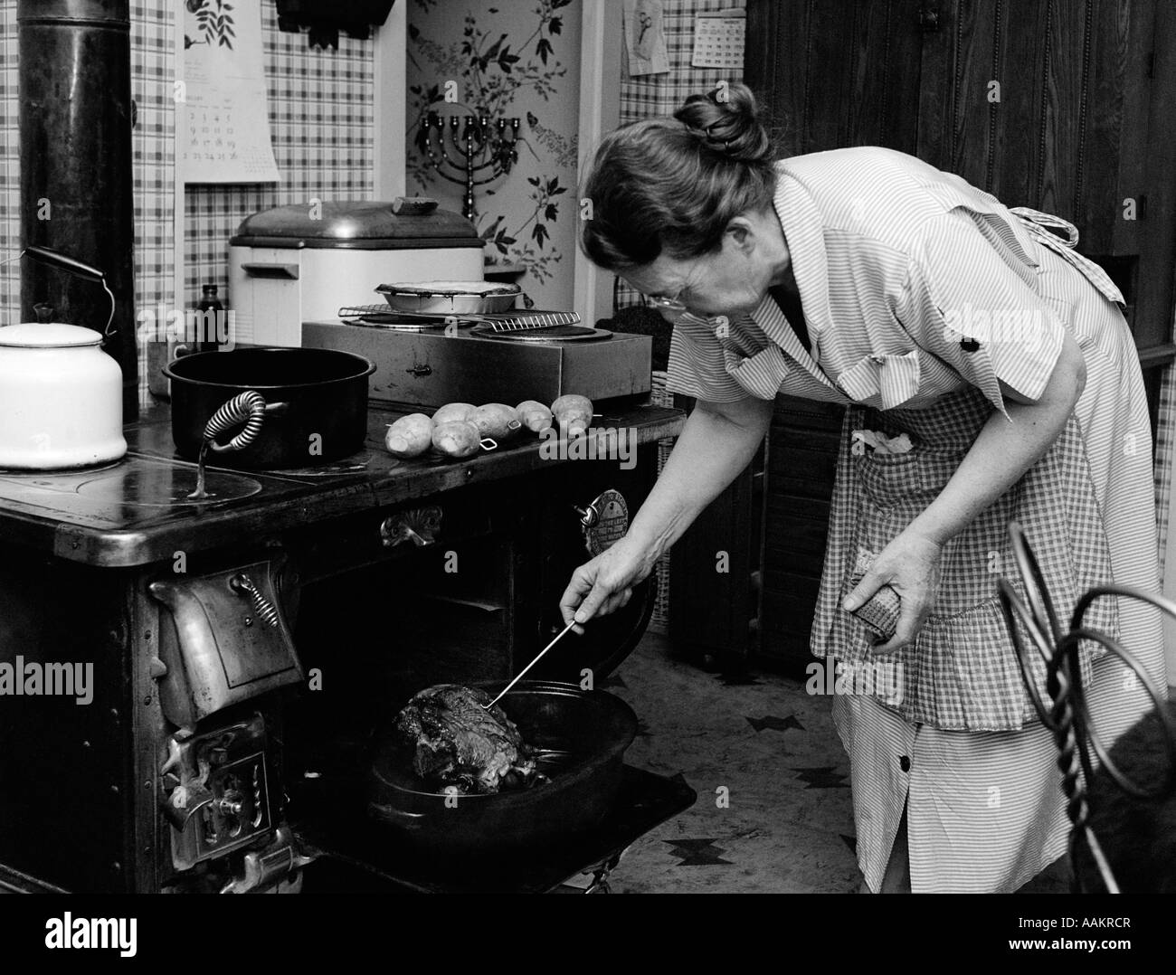 1950s HOUSEWIFE TESTING ROAST BEEF IN OVEN TO SEE IF IT IS DONE COOKING Stock Photo