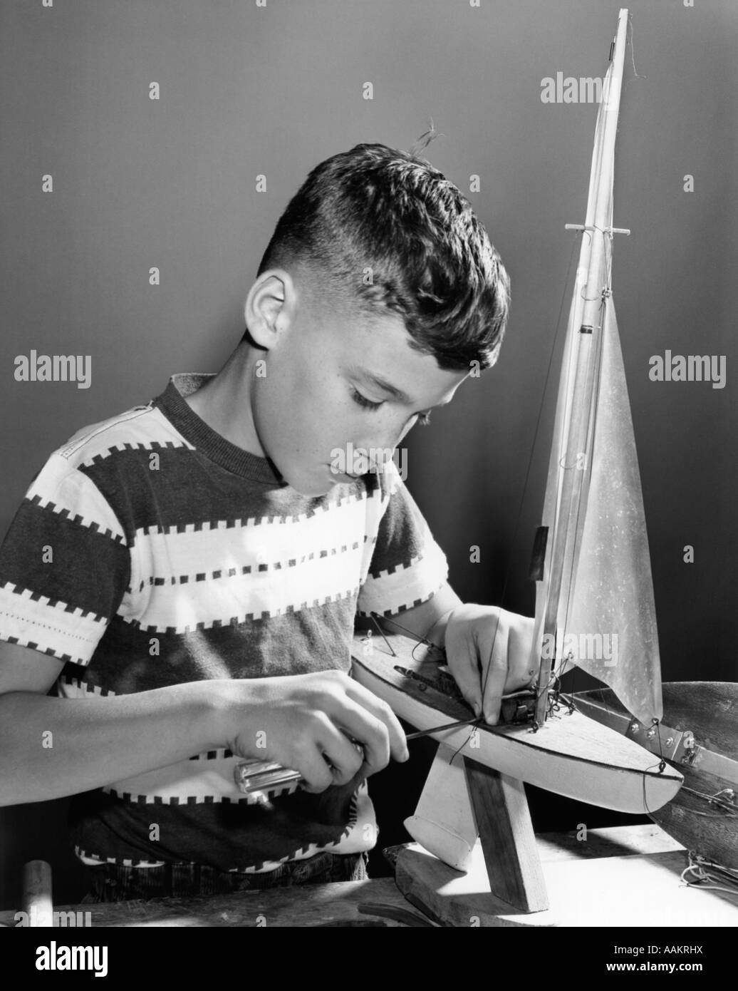 1950s BOY WORKING ON MODEL SAILBOAT Stock Photo