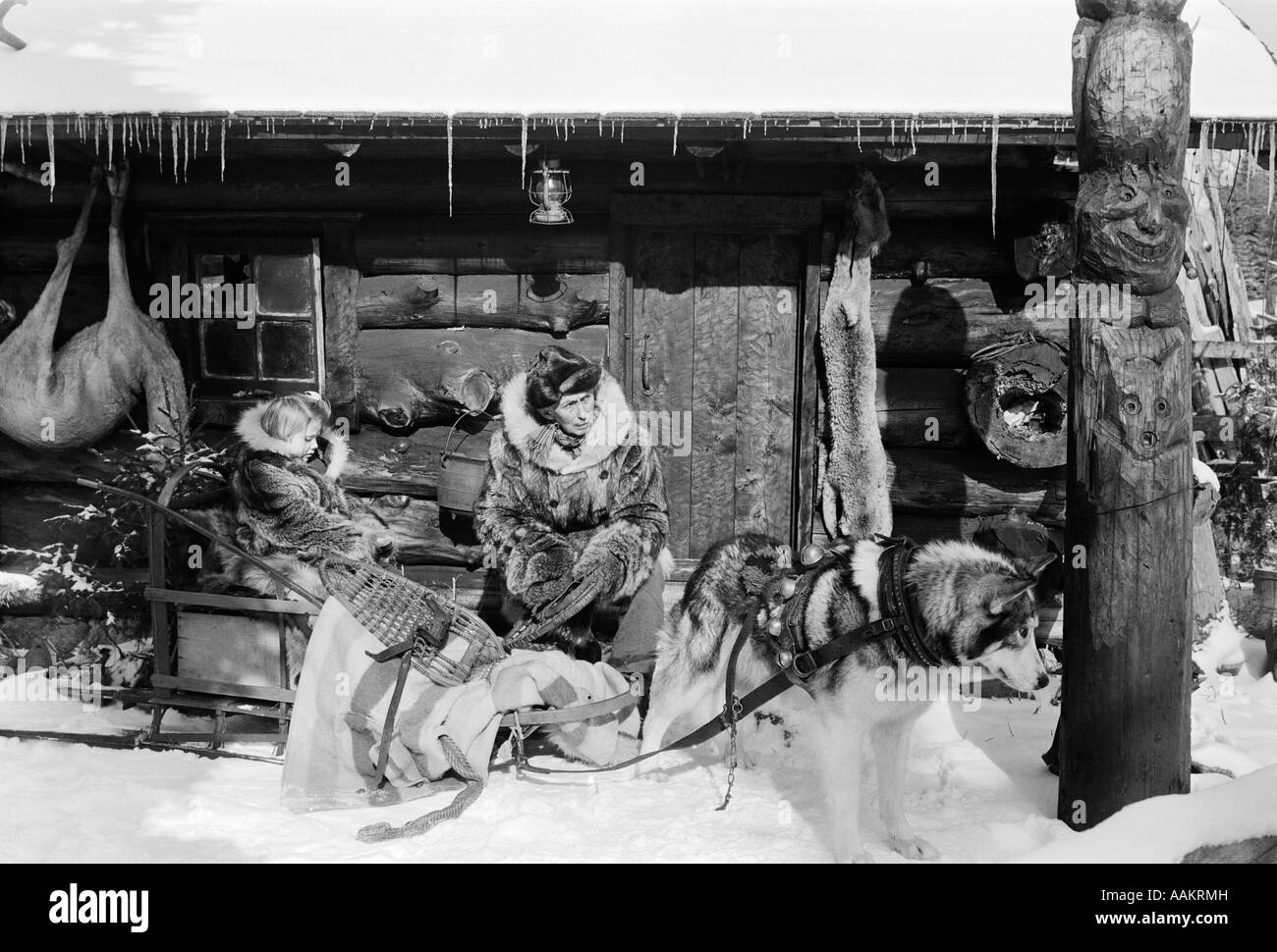 1950s HUNTERS HUNTING CABIN IN SNOW MAN DOG SLED WITH LITTLE GIRL TRAPPER FUR VINTAGE Stock Photo