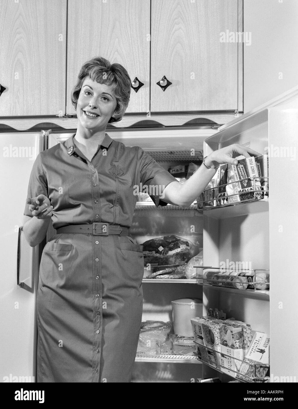1950s 1960s WOMAN HOUSEWIFE POSING BY OPEN REFRIGERATOR Stock Photo
