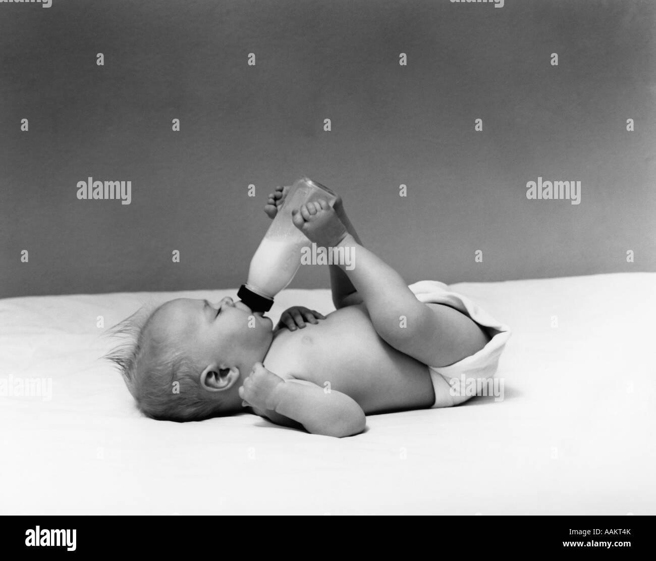1940s BABY PRONE DRINKING FROM MILK BOTTLE HELD WITH FEET Stock Photo
