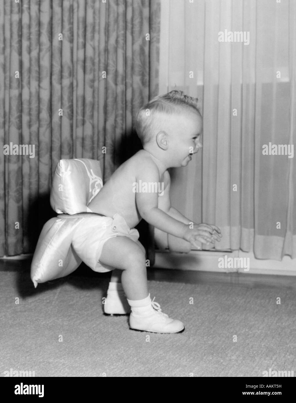 1950s LAUGHING BABY IN DIAPER AND SHOES LEARNING TO WALK WITH A PILLOW