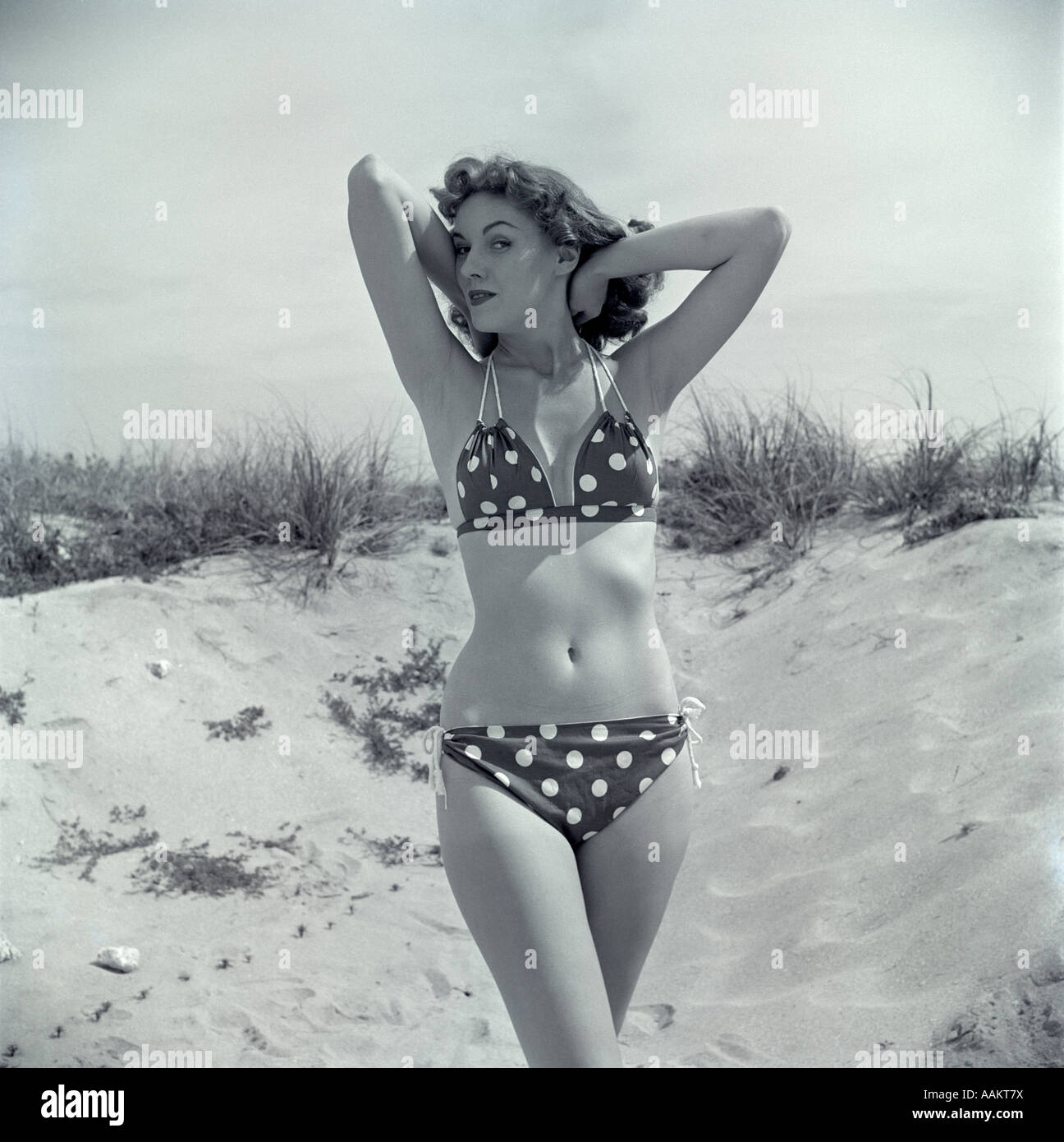 1950s BRUNETTE BATHING BEAUTY IN POLKA DOT BIKINI STANDING IN SAND WITH  HANDS BEHIND HEAD Stock Photo - Alamy