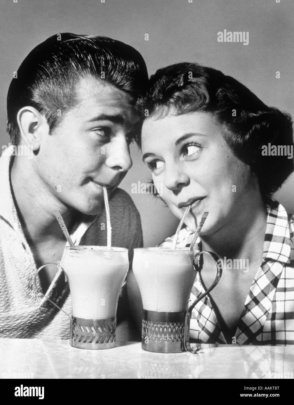1940s 1950s ROMANTIC TEENAGE COUPLE BOY AND GIRL HEAD TO HEAD DRINKING ICE CREAM SODAS Stock Photo