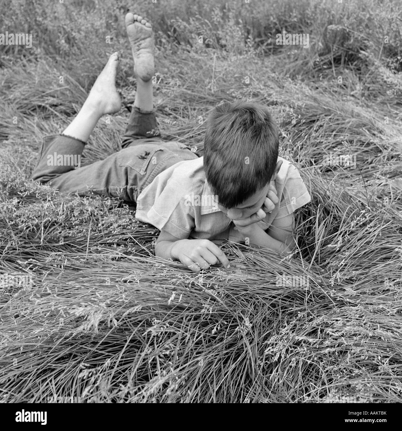 1960s BAREFOOT BOY LYING STOMACH DOWN RUNNING FINGERS THROUGH HIGH 