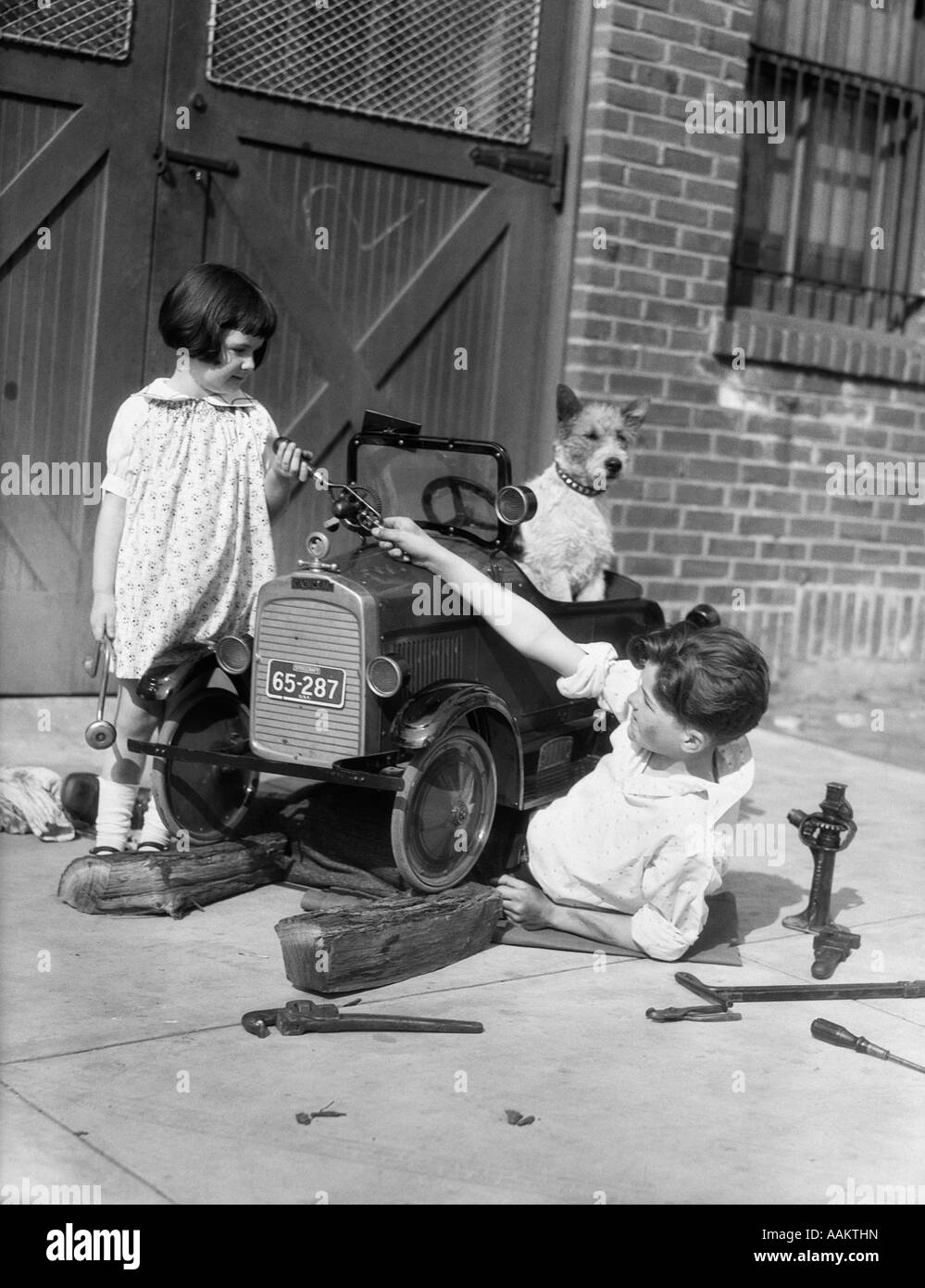 1930s TWO CHILDREN BOY GIRL AND DOG FIXING TOY AUTOMOBILE Stock Photo
