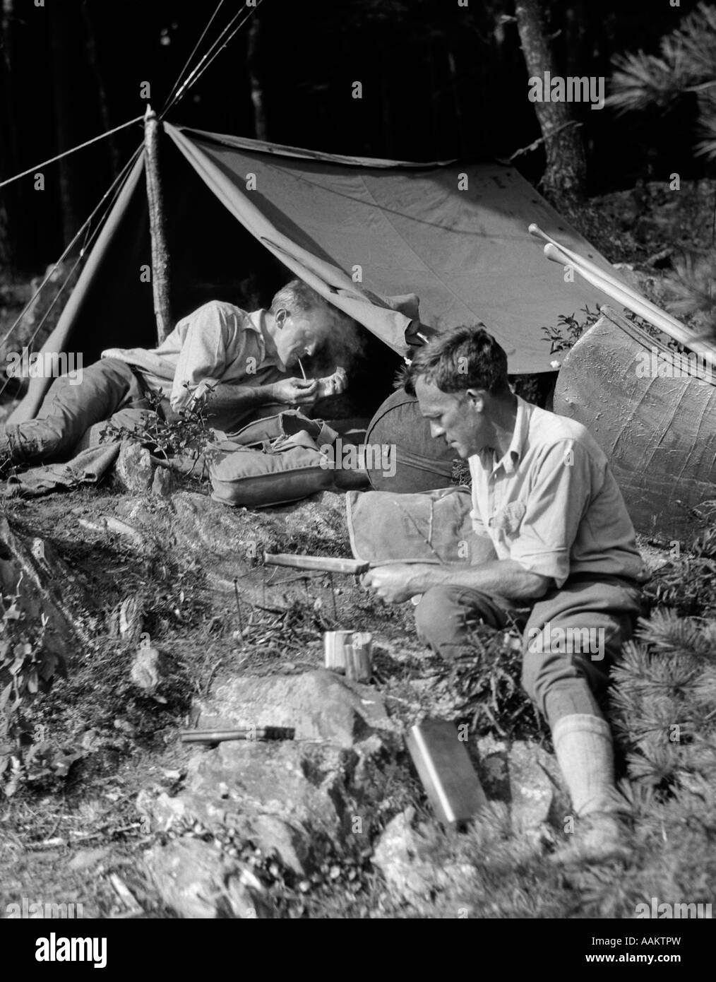 1920s TWO MEN AT PRIMITIVE CAMPSITE ONE MAN IN A FRAME TENT LIGHTING CIGARETTE Stock Photo