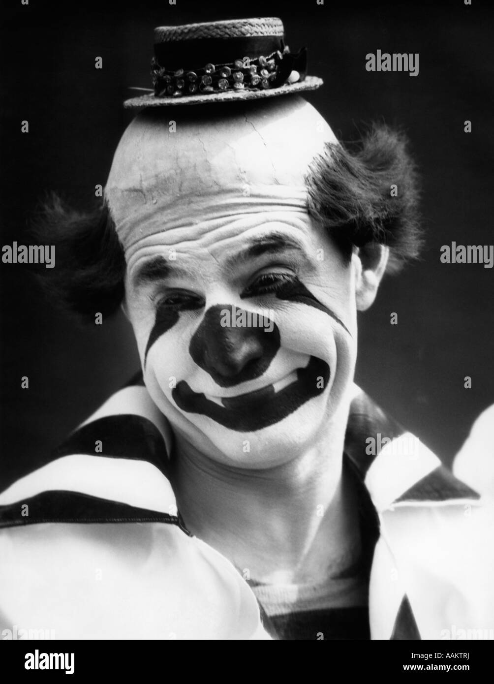 1930s CLOWN IN CLASSIC WHITEFACE WITH A HAPPY SAD FACE WITH A BALD HEAD WEARING A TINY STRAW HAT LOOKING AT CAMERA Stock Photo