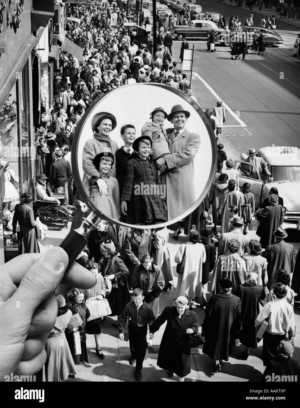 1950s MONTAGE OF FAMILY IN MAGNIFYING GLASS SUPERIMPOSED OVER CROWDED SIDEWALK Stock Photo