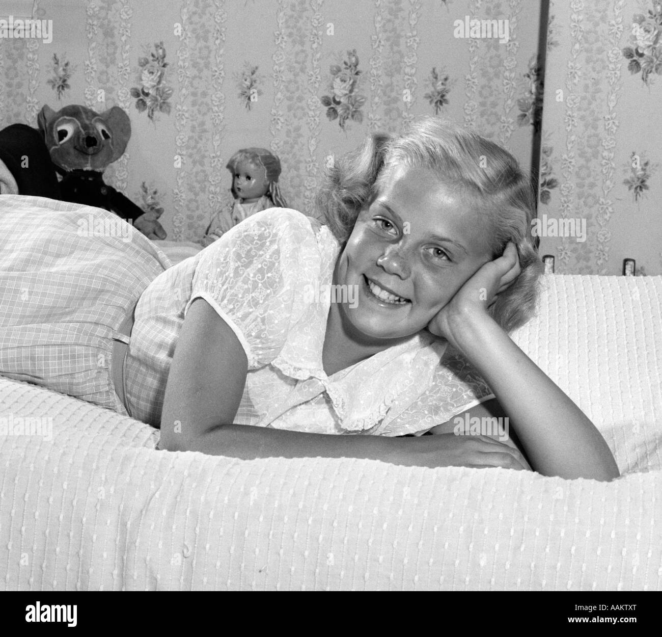 1950s YOUNG BLOND TEEN LYING ON BED SMILING HEAD RESTING ON HAND