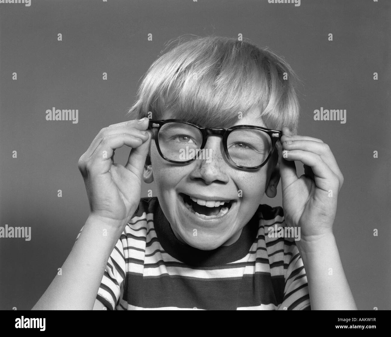 1950s 1960s SMILING LAUGHING BOY PUTTING ON ADULT EYEGLASSES Stock Photo