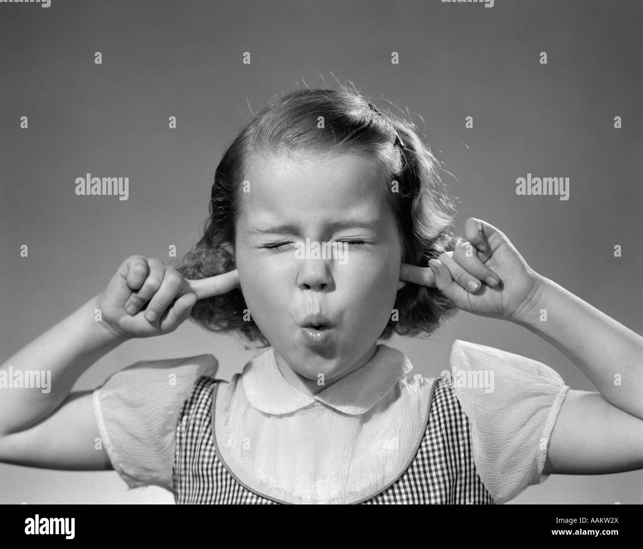 1950s GIRL WITH FINGERS IN EARS EYES CLOSED HEARING NOISE Stock Photo