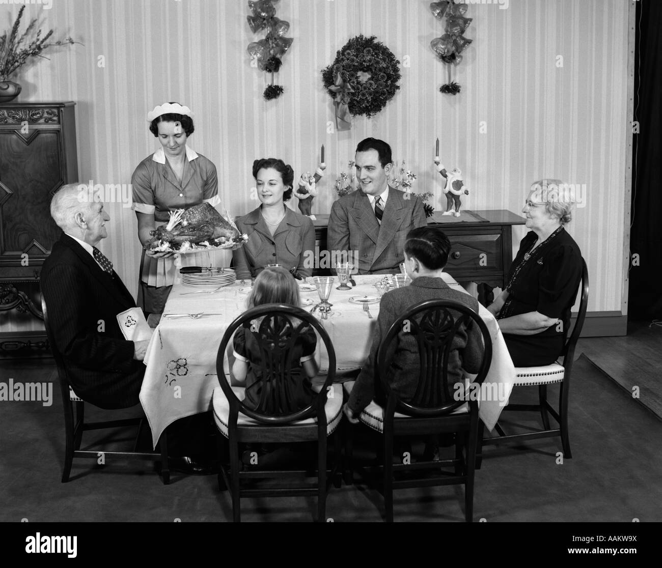 1940s THREE GENERATION FAMILY IN DINING ROOM BEING SERVED CHRISTMAS TURKEY BY MAID Stock Photo
