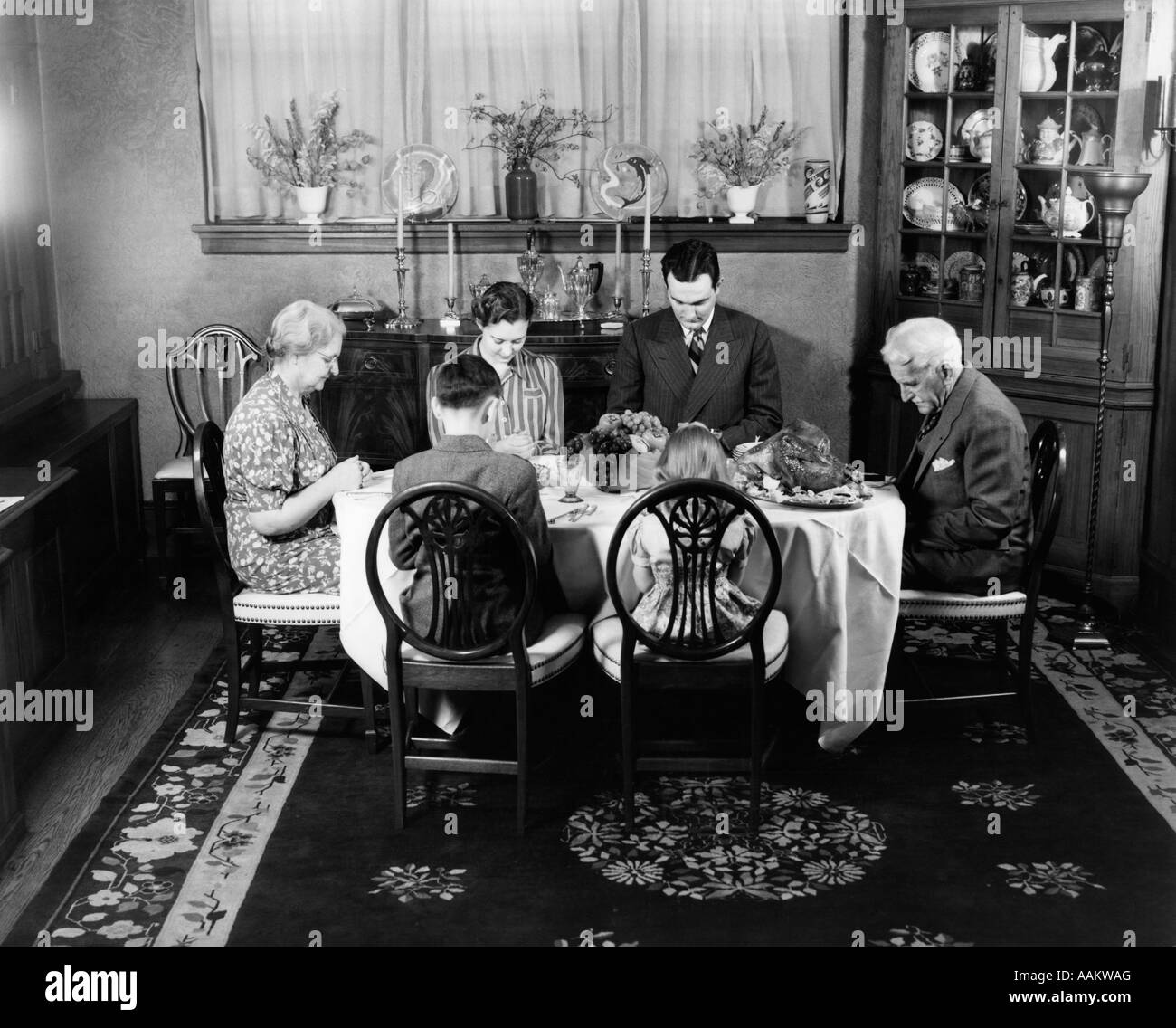 1940s EXTENDED FAMILY SITTING AROUND DINING ROOM TABLE SAYING GRACE BEFORE THANKSGIVING DINNER Stock Photo