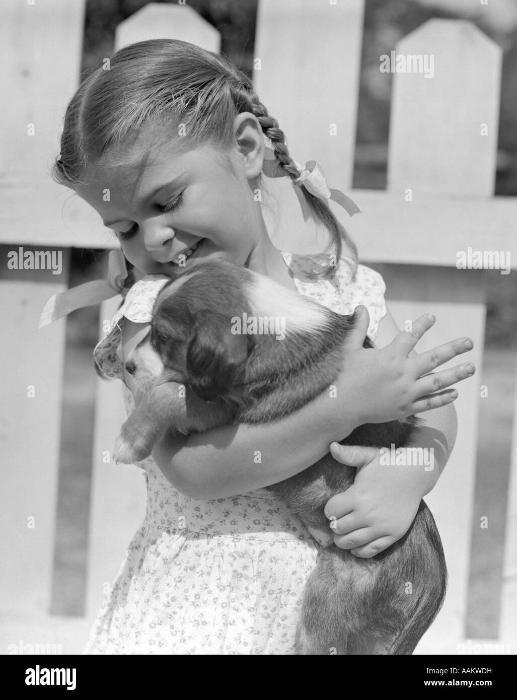 1930s 1940s 1950s LITTLE GIRL WITH BRAIDS HOLDING A NEW PUPPY DOG Stock Photo